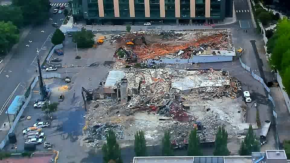 Fixed construction-camera view on June 10, 2026, showing the former low-rise buildings largely reduced to rubble with only partial walls and roof sections remaining.