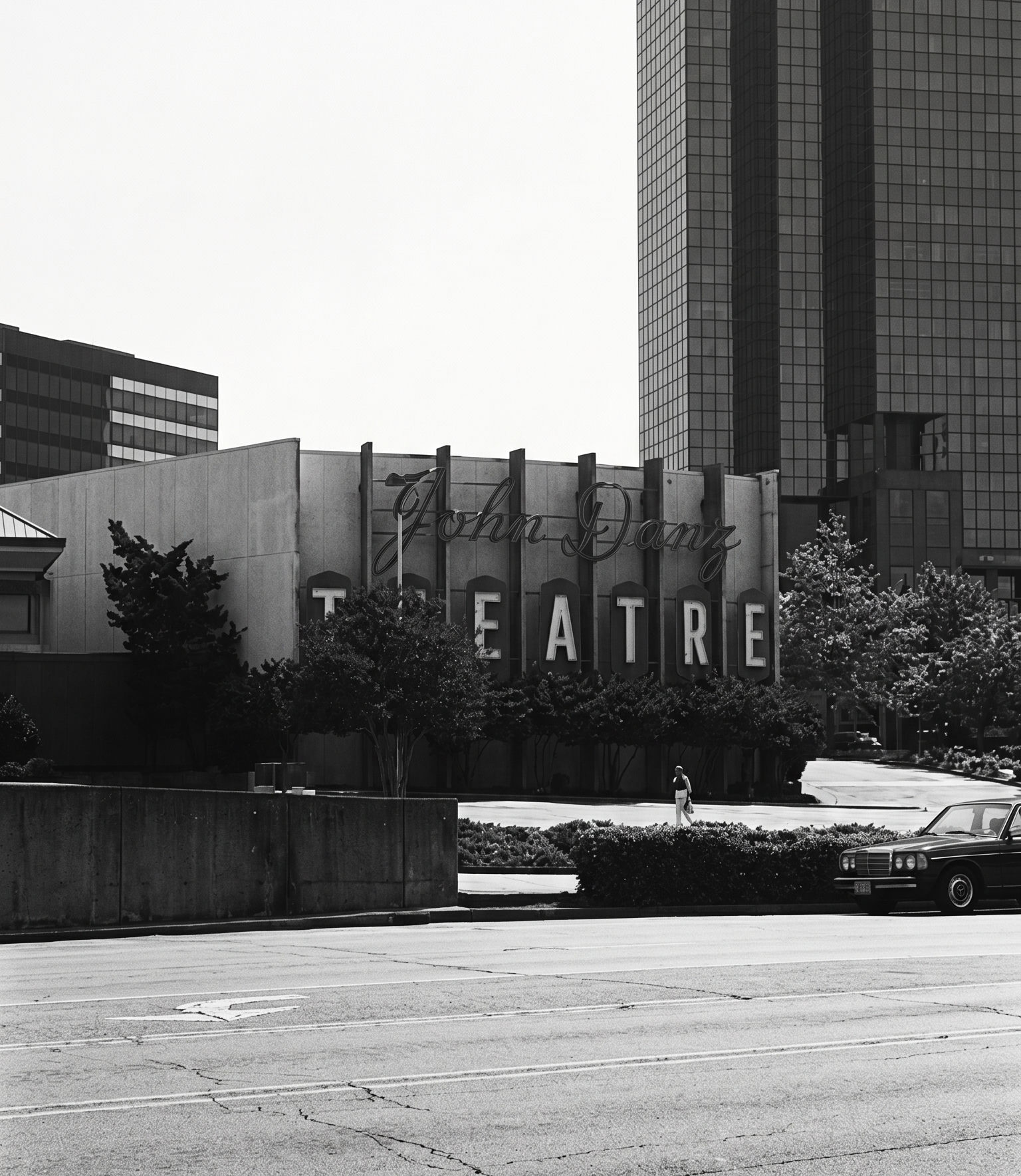 The John Danz Theatre on 106th Ave NE — the cursive 'John Danz' script above block 'THEATRE' lettering, mounted on six vertical supports, with an early Downtown Bellevue office tower rising behind.